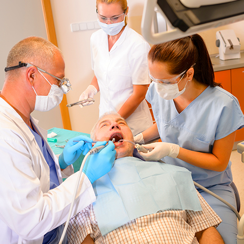 Two dental assistants making the patient comfortable in the chair while assisting dentist during oral hygiene procedure.